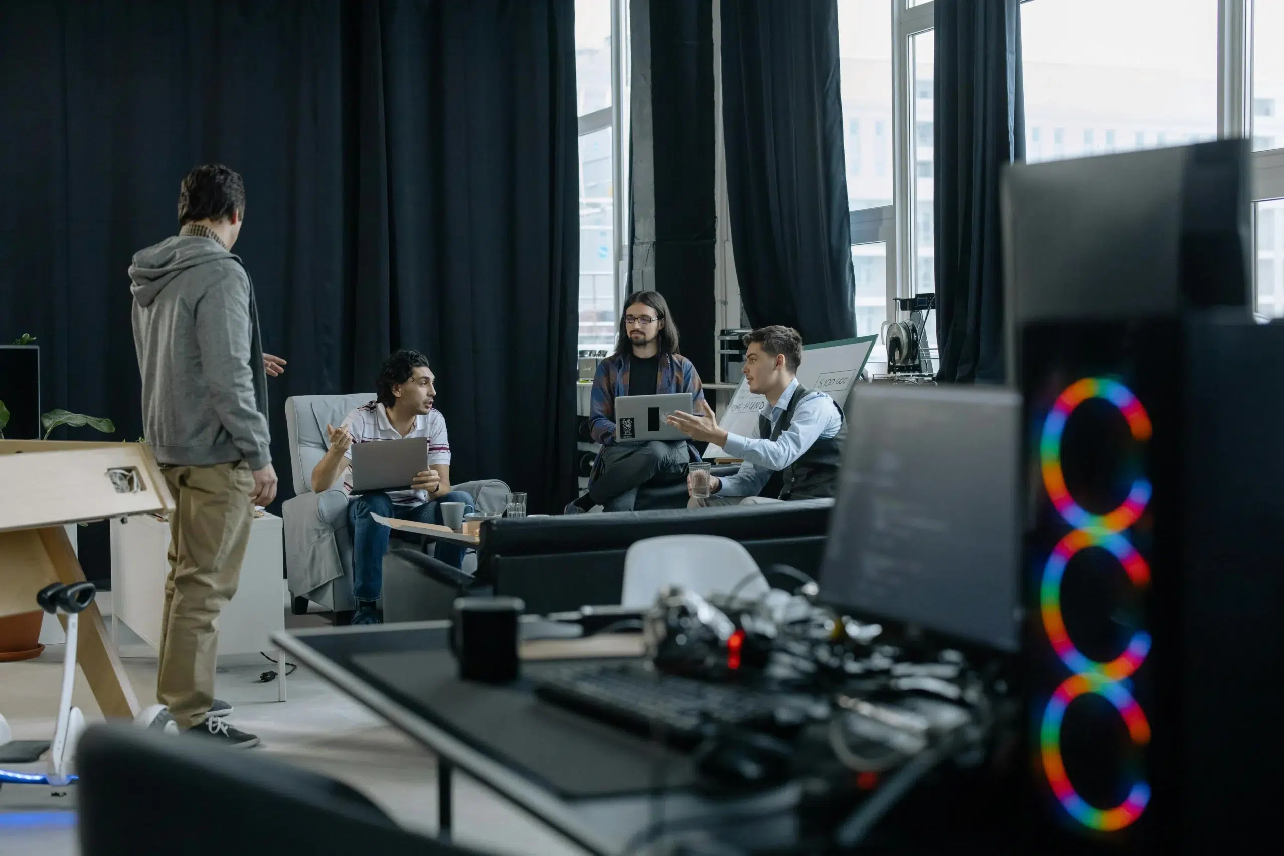 An implementation project team discussing strategy in a modern office, with stakeholders reviewing tasks on laptops and collaborating during a kickoff meeting.