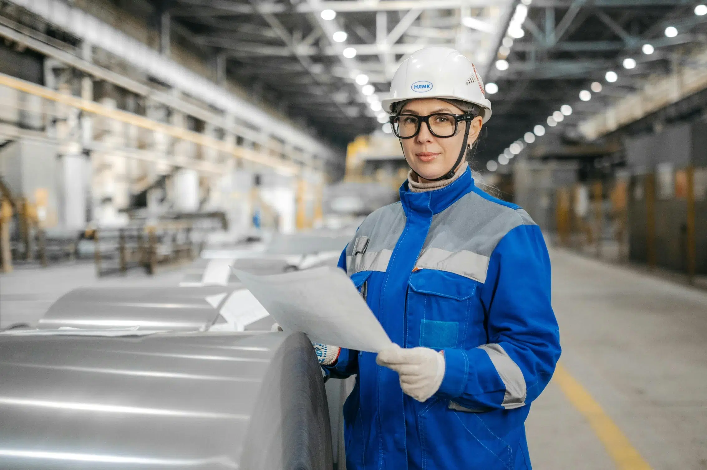 A female maintenance specialist reviewing a technical document and safety checklist near metal manufacturing equipment to ensure regulatory compliance.