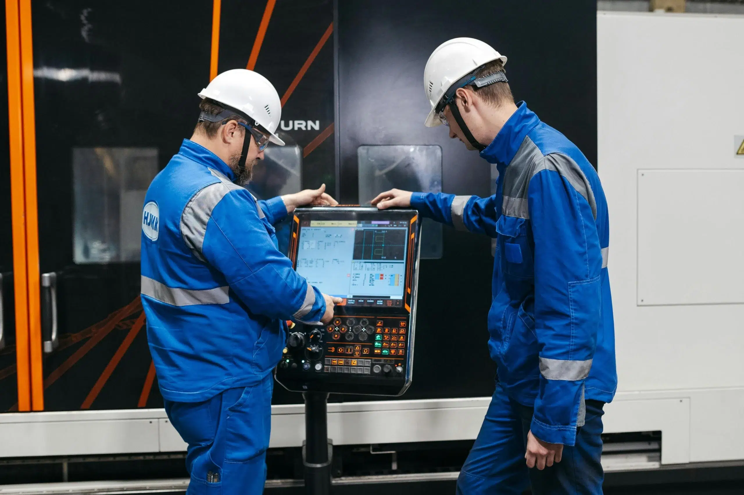 Two maintenance technicians operating a CNC machine control panel on the manufacturing floor